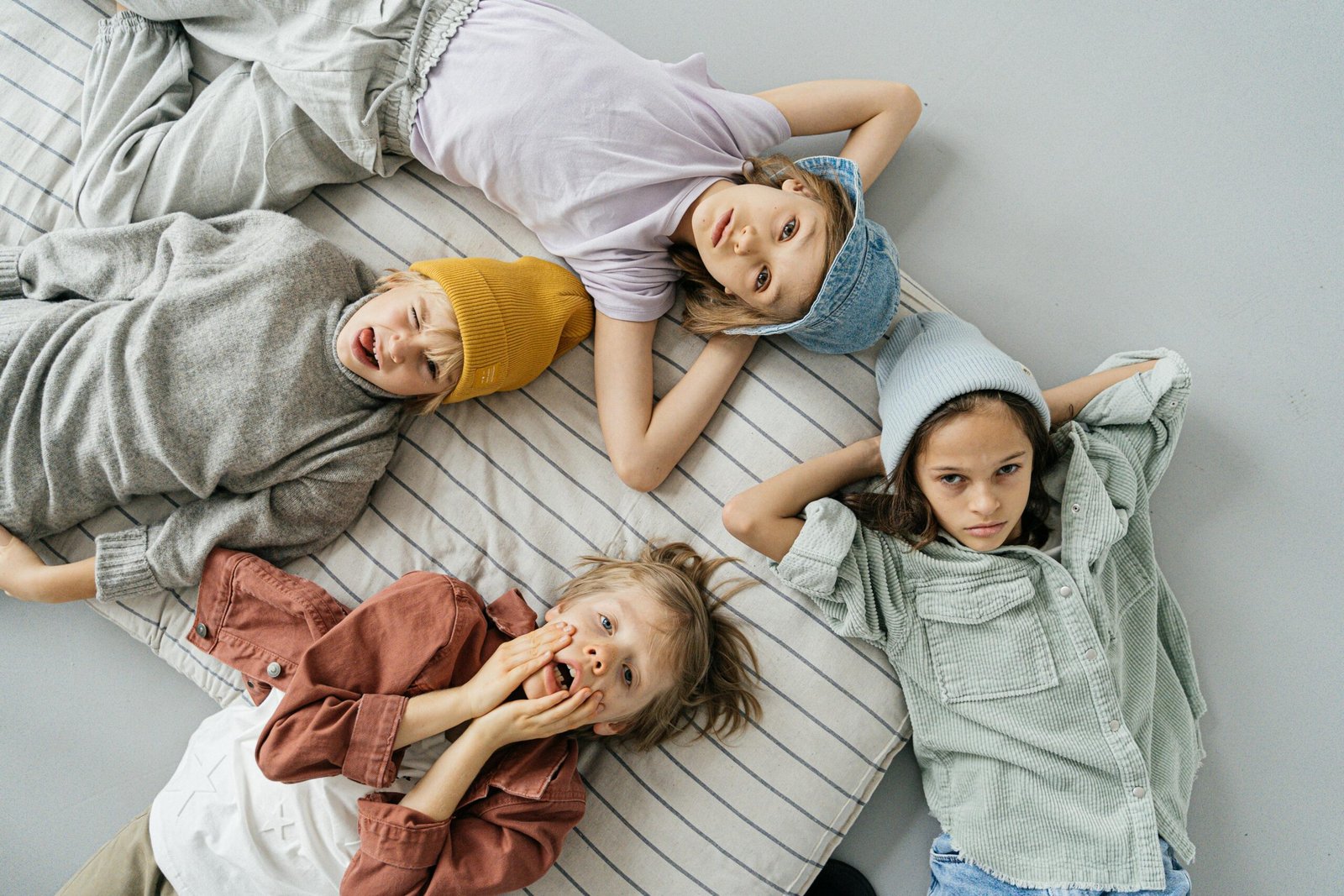 Group of four children in fashionable attire lying on a striped blanket, expressing playfulness and style.